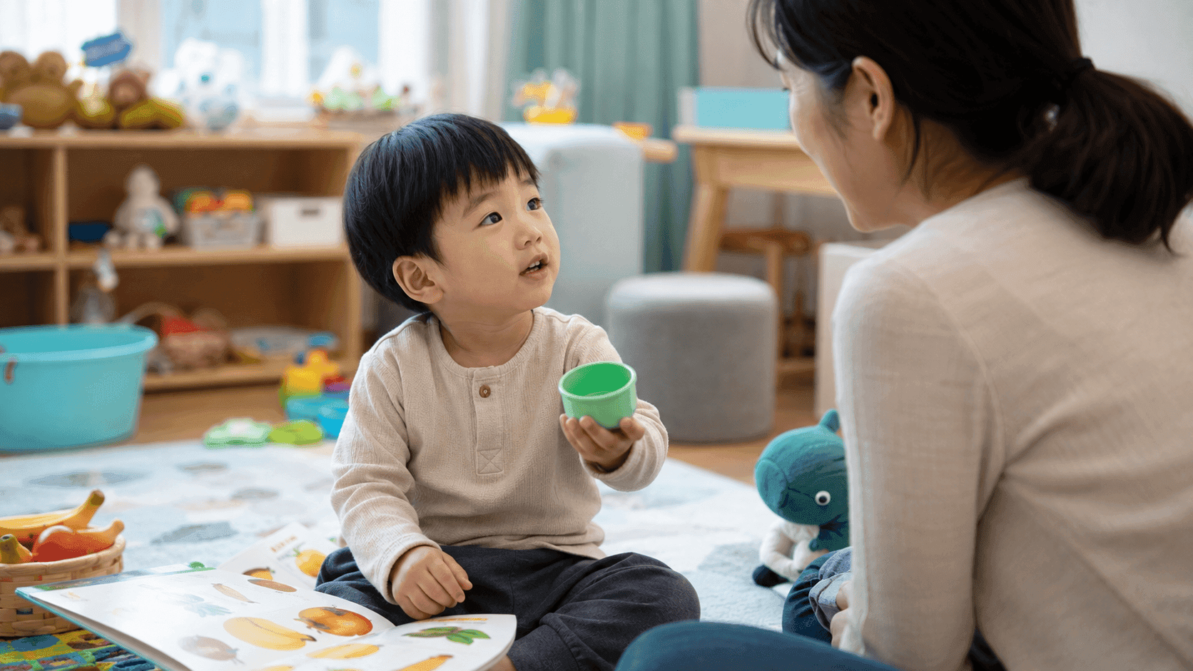 그림책과 장난감 컵을 보며 보호자에게 말하는 36개월 아이