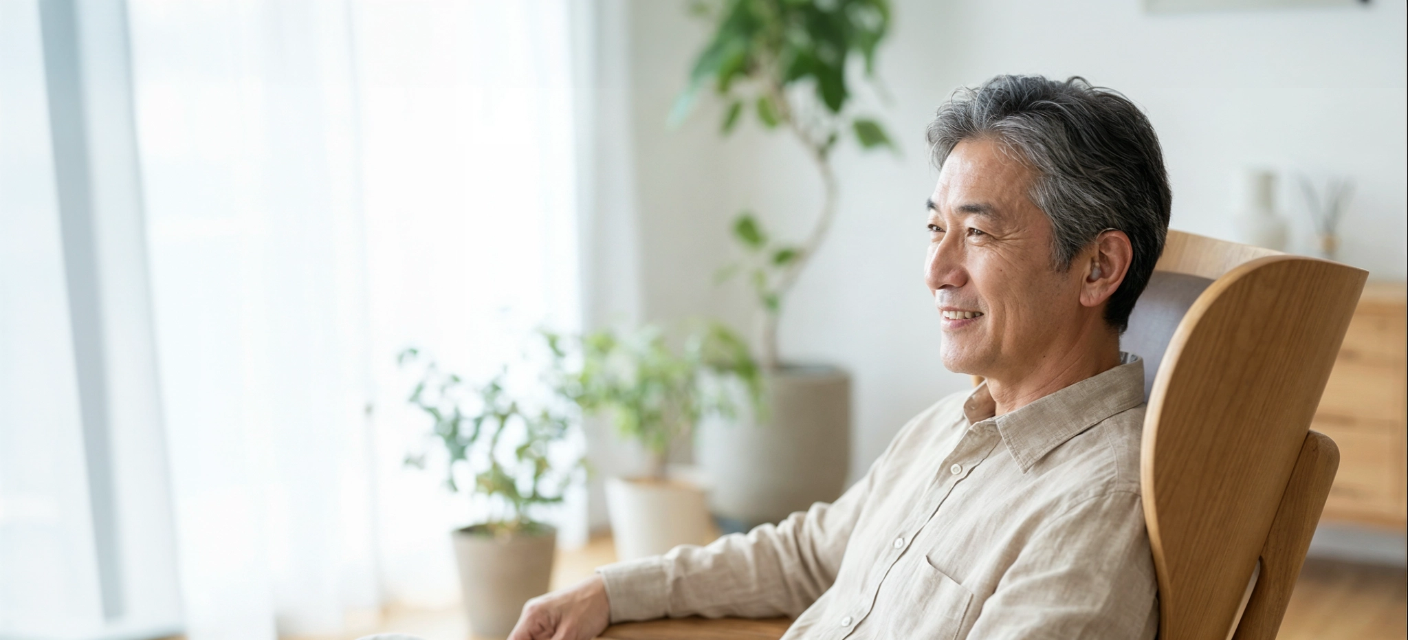 난청으로 인한 불편을 극복하고 밝은 거실에서 의자에 앉아 미소 짓는 중년 남성의 옆모습
